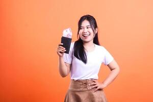 Happy woman holding a wallet filled with cash on an orange background posing with hand on hip photo