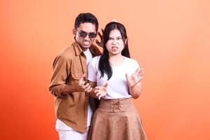a young couple asia of lovers expression annoyed to the camera where the man stands and the woman facing forward romantically. isolated on orange background photo