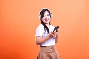 A smiling person wearing headphones holds a phone in front of an orange background photo