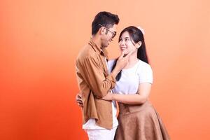 A loving couple embracing each other with orange background in the studio, looking into each other eyes photo