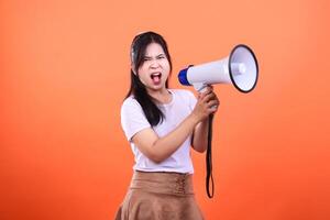 A person holds a megaphone in front of an orange background as she shouts loudly photo