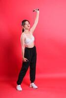 A full shot of a woman holding a jump rope with one hand overhead while the other holds the jump rope handle, isolated on a red background. photo