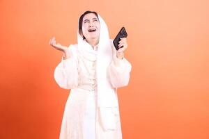 Distraught Muslim Woman with Smartphone Dramatic Expression of Disappointment, isolated on a orange background for impactful visuals. photo
