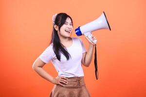 Smiling young woman using a megaphone in front of an orange background photo