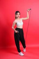 A woman is holding a skipping rope and posing for a photo, wearing sports clothing on a red background isolated on a red background photo