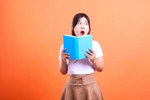 A person is holding a book with a surprised expression on her face against a solid orange background photo