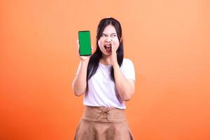 A person holding a phone with a green screen background while screaming on an orange background photo
