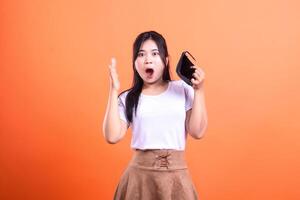 Surprised woman with empty wallet on orange background showing financial issue photo