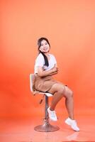 A Woman Posing on a Stool Isolated on a Vibrant Orange Background Studio Shot photo