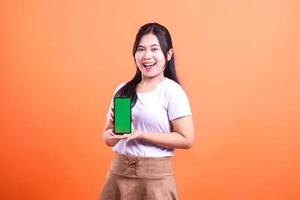 A woman holding a smart phone gadget with a green screen smiling at the camera on an orange background photo