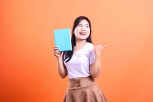 A person holding a blue book with their left hand and gesturing with their right on an orange background photo
