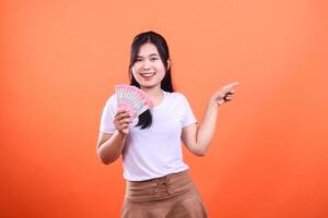 Woman holding Indonesian Rupiah bills, pointing to the side, on an orange background photo