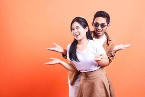 A smiling woman and a man with sunglasses are posing with open hands on orange background photo