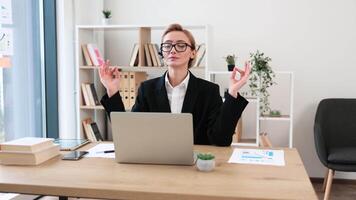 Young Caucasian female professional using a laptop, meditating while maintaining calmness in her workspace. Expressing balance and mindfulness. video