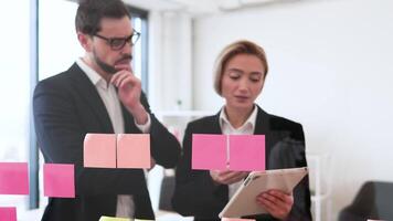 Colleagues working together on project organization using sticky notes on glass surface video