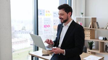 Young adult male, business professional wearing formal attire, engaging in virtual communication in modern office environment, showcasing technological interaction during work for remote collaboration video
