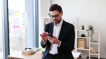 Adult male business professional interacting with smartphone in bright office with window view. video