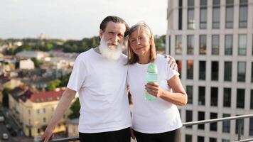 Elderly man and woman standing on rooftop smiling after morning exercise, displaying energy, health and companionship. Modern urban setting with fitness and wellness concept. video