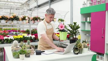 A Caucasian florist takes a photo of a potted plant, showcasing a flower in a bright shop setting with flowers. video