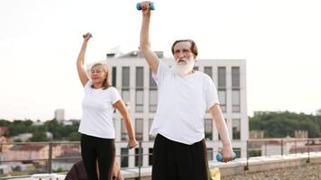 Elderly man and woman exercising with dumbbells outside. Promotes healthy lifestyle, fitness, exercise. They appear happy and engaged, emphasizing wellness, activity, and staying active at any age. video