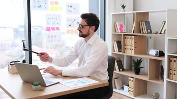 Smiling young adult male professional workplaces creating business content with smartphone in office. Displays productive working environment, successful interaction, digital recording. video