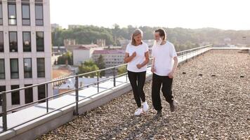 Senior man with beard and woman jogging together on urban rooftop during daytime. Active lifestyle for older adults promoting health and companionship. video