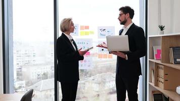 Two business professionals, man and woman, shaking hands, discussing work in bright office setting video