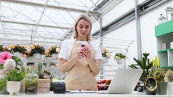 A Caucasian woman in an apron uses a phone at a desk in a florist shop. She's writing something while in a conversation. video