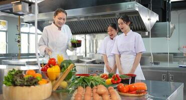 Culinary Students Practicing Cooking Skills with Instructor, Young Chefs Learning and Cooking in a Professional Kitchen, Young Female Cooks Preparing Food in a Commercial Kitchen photo
