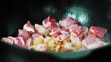 Searing red meat pieces sizzling in hot oil within dark cast iron cauldron, releasing fragrant steam and creating rich, golden brown surface during culinary preparation video