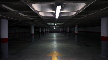 Dim underground parking garage with flickering fluorescent lights revealing grey concrete columns and empty floor. Creating mysterious industrial atmosphere through shadowy architectural perspective video