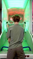 Teenage player standing near arcade basketball machine, intensely focusing while aiming and throwing ball with precise hand eye coordination in brightly colored gaming environment video