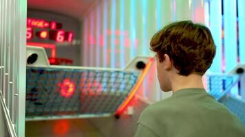 Young male confidently playing fast paced basketball arcade game, demonstrating hand eye coordination and competitive spirit under vibrant neon illumination in dimly lit game room video