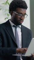 Vertical view African American pensive worry business man in office using laptop chatting typing online work trouble think solution difficult job ethnic male businessman guy worker looking out window video