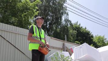 Construction Worker Operating Remote Control Device, Safety vest and cap under power lines at building site with materials video