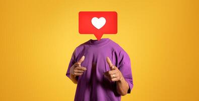 A person dressed in a purple shirt points towards the viewer, their head replaced with a large heart icon. The bright yellow background emphasizes the theme of social media positivity and interaction. photo