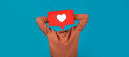 A person sits back with arms behind their head, appearing relaxed. Above them is a prominent red speech bubble with a white heart icon, showcasing a connection to social media. photo