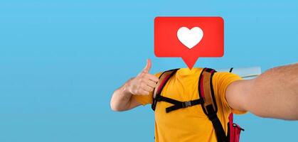 A backpacker in a yellow shirt poses against a bright blue background. They give a thumbs-up while a heart icon floats instead of head, showcasing their enthusiasm for travel and social media photo