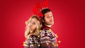 Unhappy millennial couple tied with Christmas lights on red background photo