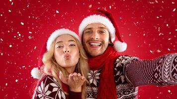 Affectionate millennial couple in Christmas clothes taking selfie together on red background photo