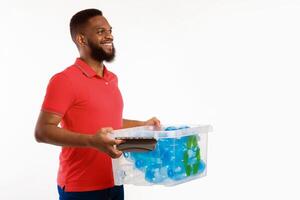 Recycle And Sort Your Waste. Side View Of Black Guy Holding Box With Recycling Sign Full Of Used Plastic Litter And Bottles Posing In Studio On White Background. Free Space For Text photo