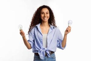 Save Energy. Cheerful Lady Holding Two Lightbulbs Choosing Energy Saving Light Bulb Standing Over White Studio Background, Looking At Camera. Safe Light-Bulbs Disposal Service Concept photo