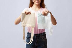 Zero Waste Shopping Concept. Unrecognizable Woman Holding Reusable Eco Bag In One Hand And Plastic Polyethylene Bag In Another While Standing Over Gray Studio Background, Cropped Image, Closeup photo