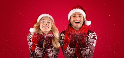 Christmas time. Happy millennial guy and his girlfriend blowing snow on red background photo