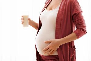 Unrecognizable Pregnant Woman With Glass Of Milk In Hands Standing Near Window And Touching Her Belly, Young Expectant Mother Enjoying Healthy Calcium Drink, Cropped Image With Copy Space photo