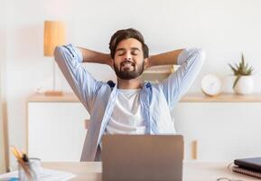 Smiling Arab Freelancer Guy Leaning In Chair, Relaxing At Workplace After Working Remotely On Laptop In Home Office, Happy Successful Eastern Man Enjoying Distant Job Opportunities, Free Space photo
