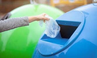 Zero Waste Concept. Unrecognizable woman throwing single use plastic bag into blue recycle bin outdoors, sorting garbage to different trash containers, cropped image with selective focus, panorama photo