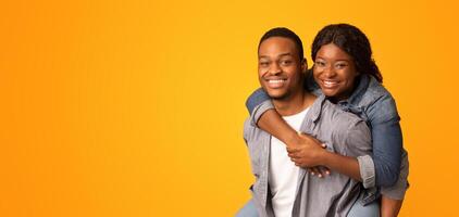 Cheerful Romantic Black Couple Having Fun Together, Loving African American Guy Piggybacking His Girlfriend, Cheerful Lovers Fooling Over Yellow Background, Enjoying Time With Each Other, Copy Space photo