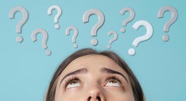Young woman looking up at question marks, representing thought and inquiry photo