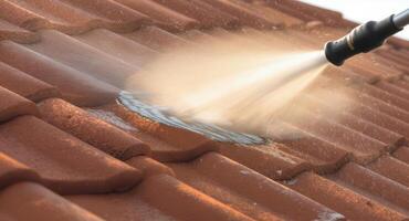 Close up of a power washer cleaning a dirty terracotta tile roof, removing grime and moss during house maintenance. photo